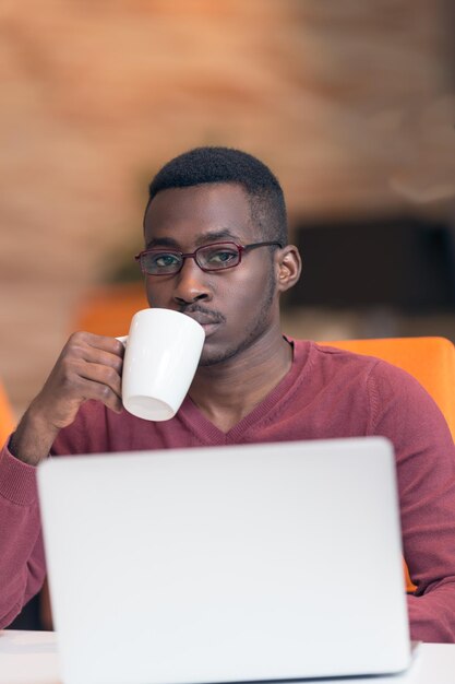 Fröhlicher junger afrikanischer Geschäftsmann, der auf dem Laptop tippt