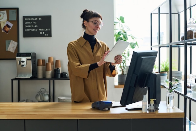 Fröhlicher junger Angestellter des Cafés, der Daten in das Tablet am Schalter eingibt