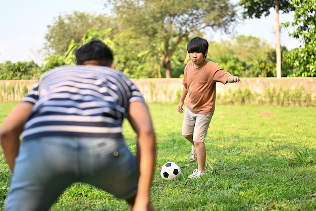 Fröhlicher junger asiatischer Junge, der mit seinem Vater im Hinterhof Fußball spielt und gemeinsam Spaß hat