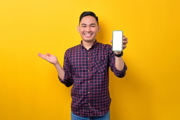 Fröhlicher junger asiatischer Mann, der ein Smartphone mit leerem Bildschirm hält, isoliert auf gelbem Hintergrund Werbung für ein neues Mockup-Konzept für mobile Apps