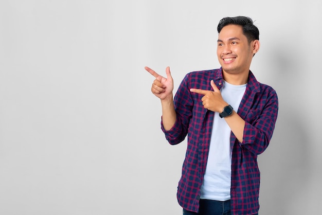 Fröhlicher junger asiatischer Mann im karierten Hemd, der mit dem Finger auf das Werbebanner des Kopierraums zeigt, das auf weißem Hintergrund isoliert ist