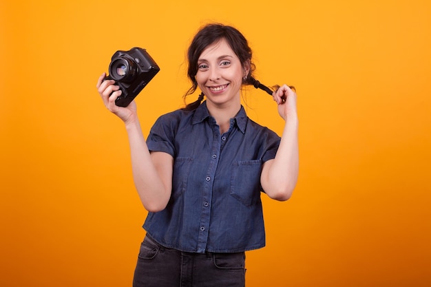 Fröhlicher junger Fotograf mit Kamera in der Hand über gelbem Hintergrund im Studio. Moderne Technik für Fotografen.