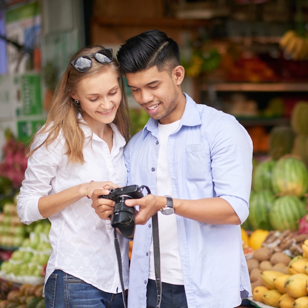 Fröhlicher junger Freund und Freundin überprüfen Fotos, die sie während des Urlaubs mit der Digitalkamera gemacht haben