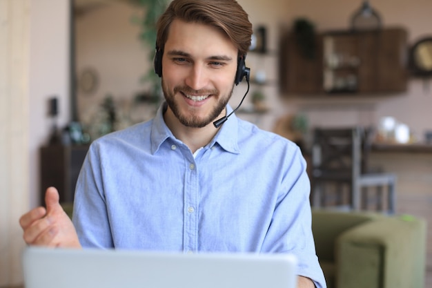 Fröhlicher junger männlicher Support-Telefon-Operator im Headset, am Arbeitsplatz bei der Verwendung von Laptop, Hilfsdienst und Kundenberatungs-Call-Center-Konzept.