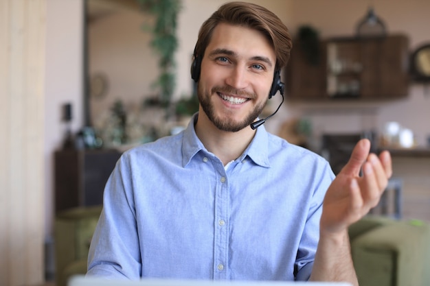 Fröhlicher junger männlicher Support-Telefon-Operator im Headset, am Arbeitsplatz bei der Verwendung von Laptop, Hilfsdienst und Kundenberatungs-Call-Center-Konzept.