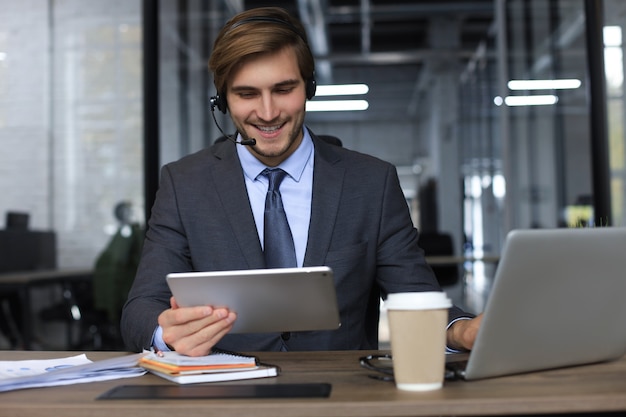 Fröhlicher junger männlicher Support-Telefon-Operator im Headset, am Arbeitsplatz bei der Verwendung von Laptop, Hilfsdienst und Kundenberatungs-Call-Center-Konzept.