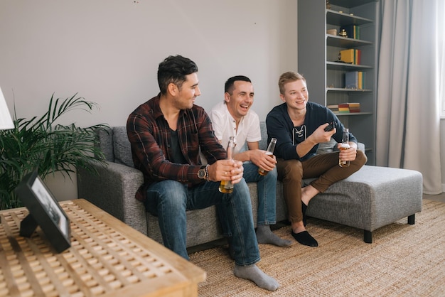 Fröhlicher junger Mann, der fernsieht Eine Gruppe von Freunden verbringt abends Zeit zusammen hinter dem Fernseher