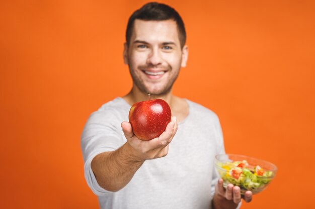 Fröhlicher junger Mann, der gesunden Salat und Früchte isst