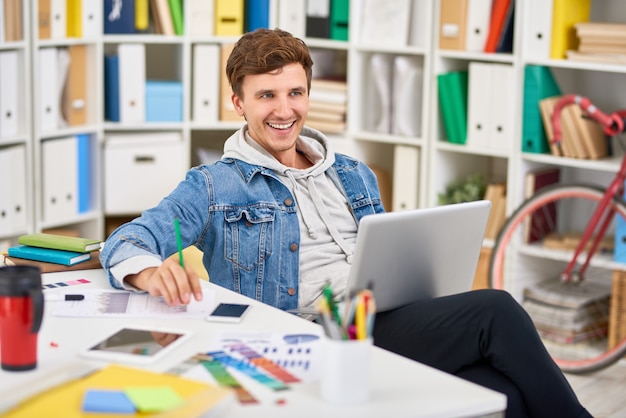 Fröhlicher junger Mann, der im Büro arbeitet