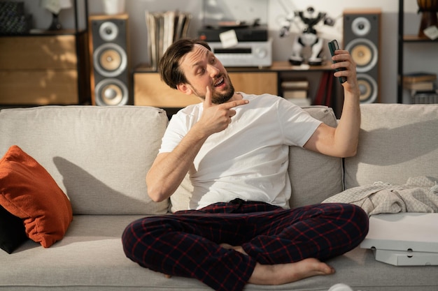 Fröhlicher junger Mann kommuniziert über Skype mit seinen Freunden, die er auf der Couch sitzt