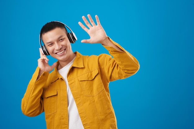 Fröhlicher junger Mann mit Kopfhörern, der Musik hört und mit der Hand winkt