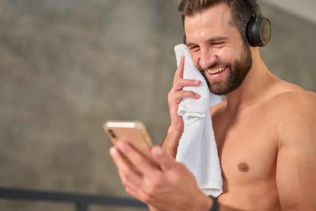 Fröhlicher junger Mann mit modernem Smartphone nach dem Training