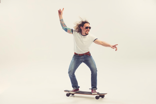 Fröhlicher junger Mann Skateboarding isoliert über weißem Studiohintergrund Retro-Stil