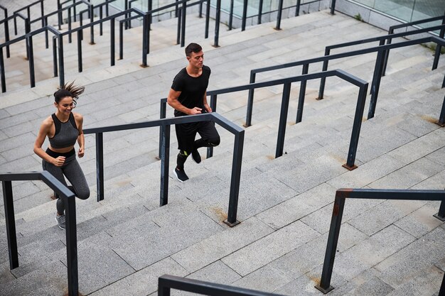 Fröhlicher junger Mann und Frau, die Cardio-Training machen und im Stadtzentrum nach oben laufen?