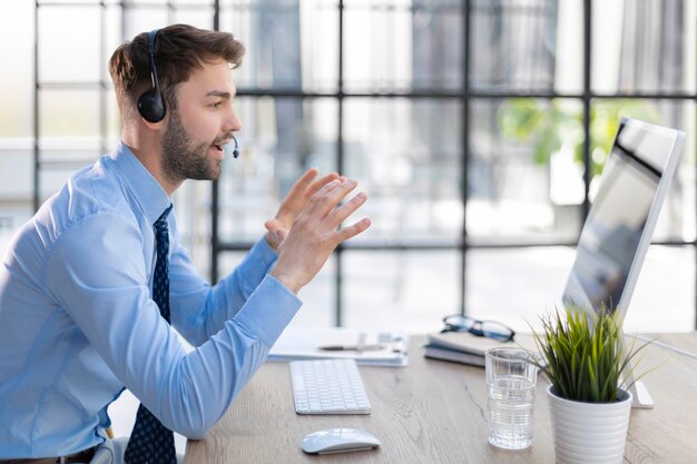 Fröhlicher junger Support-Telefon-Operator im Headset am Arbeitsplatz bei der Verwendung des Computers