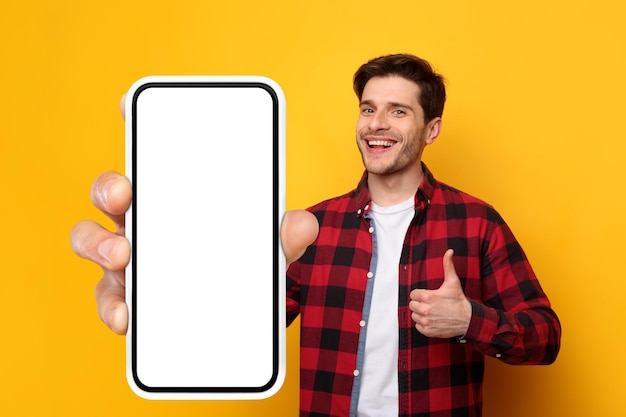 Fröhlicher Kerl, der großen weißen leeren Smartphone-Bildschirm und dergleichen zeigt