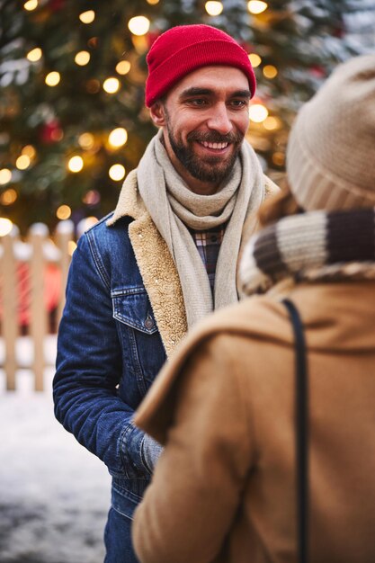 Fröhlicher Kerl, der während der Winterferien mit einer Frau im Freien spazieren geht