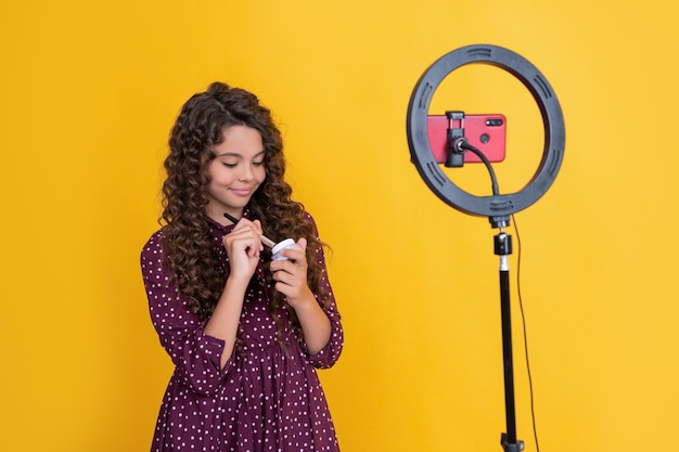 Fröhlicher Kinderblogger mit langen lockigen Haaren, der ein Video für einen Blog-Hold-Pulverpinsel macht