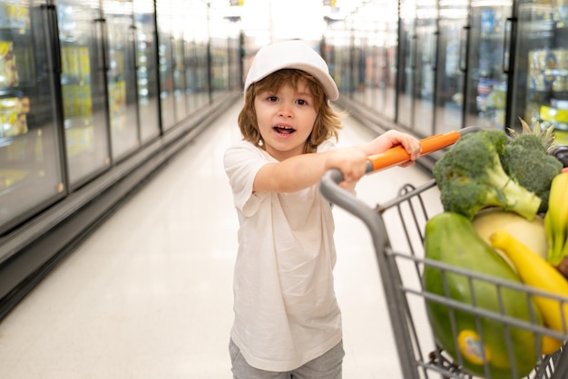 Fröhlicher Kinderjunge im Supermarkt kauft Gemüse, gesundes Essen für Kinder, lustiges Einkaufen, süßes Kind wi