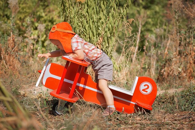 Fröhlicher Kinderjungenpilot, der im Sommer mit rotem Spielzeugflugzeug sitzt und spielt Träume Kind der Reise