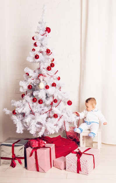 Fröhlicher kleiner Junge, der nahe Weihnachtsbaum spielt