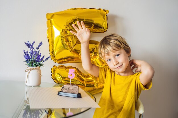 Fröhlicher kleiner Junge, der seinen Geburtstag feiert und Kerzen auf hausgemachtem Kuchen im Innenbereich bläst Geburtstagsfeier für Kinder Unbeschwertes Jubiläumsglück in der Kindheit Fünf Jahre alt