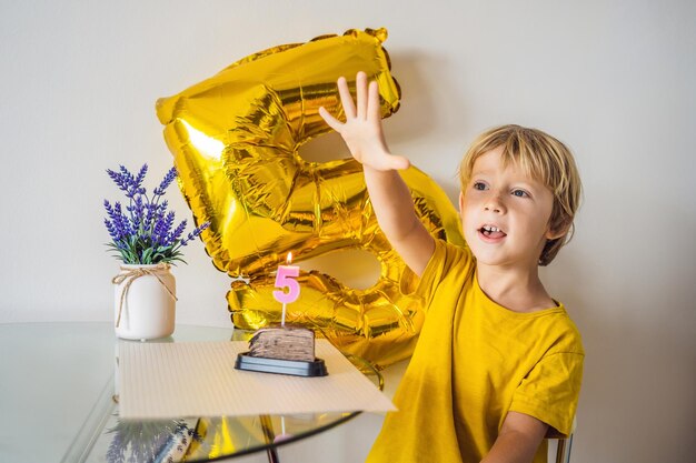 Fröhlicher kleiner Junge, der seinen Geburtstag feiert und Kerzen auf hausgemachtem Kuchen im Innenbereich bläst Geburtstagsfeier für Kinder Unbeschwertes Jubiläumsglück in der Kindheit Fünf Jahre alt