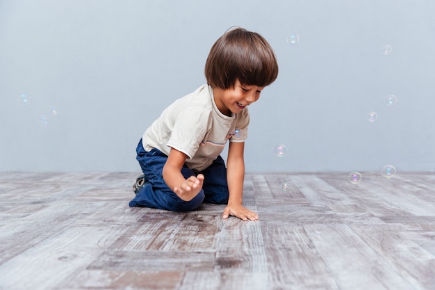 Fröhlicher kleiner Junge sitzt und spielt mit Seifenblasen