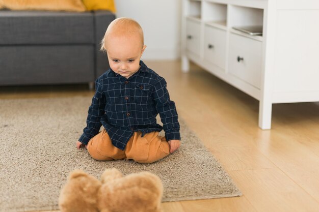 Fröhlicher Kleinkindjunge, der mit ihrem Teddybären im Haus spielt Kindheits- und Entwicklungsstadien des Kindes