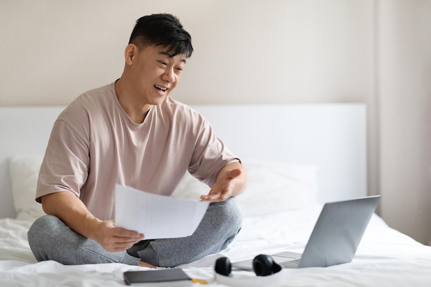 Fröhlicher koreanischer Geschäftsmann hat Online-Meeting-Hotelzimmer-Interieur