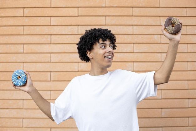 Fröhlicher lächelnder Afroamerikaner in einem weißen T-Shirt mit Schokolade und blauen Donuts