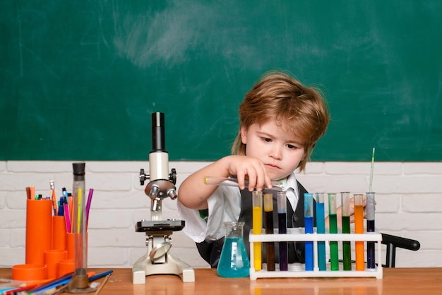 Fröhlicher lächelnder kleiner Junge, der Spaß gegen Wissenschafts- und Bildungskonzept der ersten Klasse der blauen Wand hat m