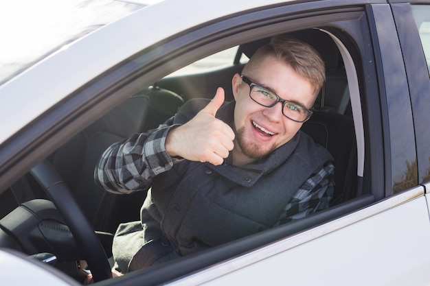 Fröhlicher lässiger Kerl, der glücklich lächelnd zeigt Daumen hoch sitzend in einem großen weißen Auto