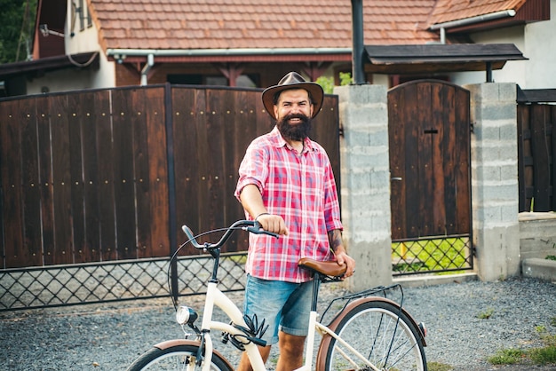 Fröhlicher Landmann. Hübscher junger Mann, der beim Fahrradfahren im ländlichen Dorf lächelt.