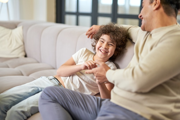 Fröhlicher lateinamerikanischer Junge, der Spaß hat, während er Zeit mit seinem Vater verbringt und zu Hause im Wohnzimmer spielt. Familie, Freizeit, Vaterschaftskonzept