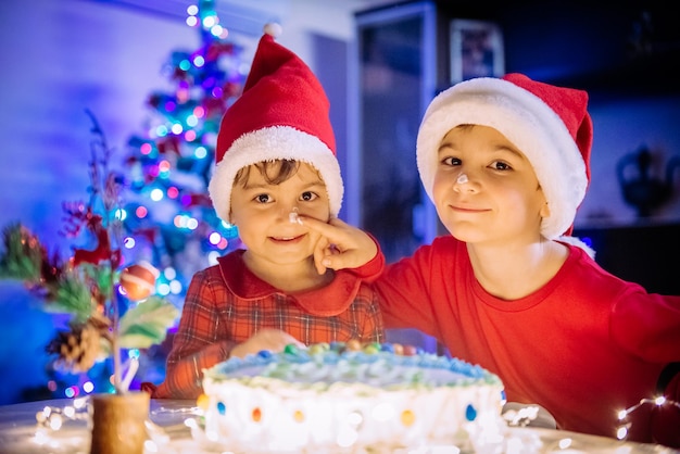 Fröhlicher lustiger Kinderjunge und -mädchen mit Smiley-Gesicht mit Kuchen auf der Neujahrsparty zu Hause