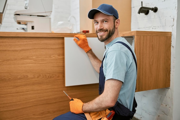 Foto fröhlicher männlicher arbeiter, der die schranktür in der küche repariert