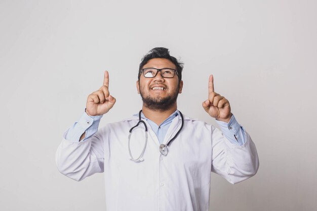 Fröhlicher männlicher Arzt, der mit beiden Händen nach oben zeigt, isoliert auf weißem Hintergrund
