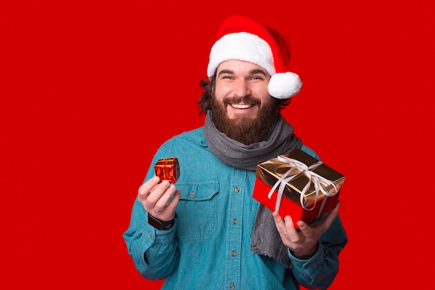 Fröhlicher männlicher Hipster hält zwei Geschenke für eine Weihnachtsfeier.