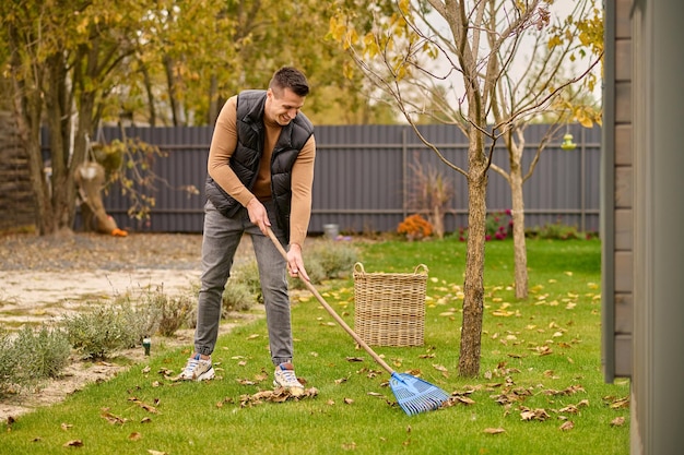 Fröhlicher Mann, der Blätter mit Gartenwerkzeugen schaufelt