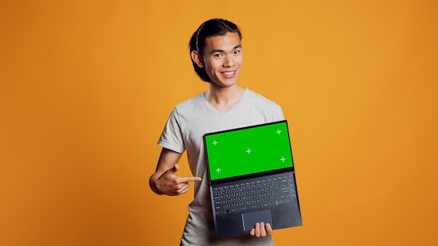 Fröhlicher Mann, der einen Laptop mit Greenscreen vor der Kamera hält und eine isolierte Anzeigevorlage zeigt. Fröhlicher moderner Typ, der leere Chroma-Schlüssel und Mockup auf dem PC-Bildschirm betrachtet, moderner Copyspace.