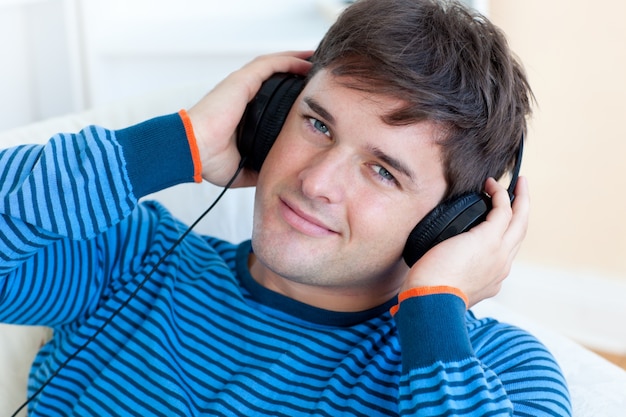 fröhlicher Mann, der Musik mit Kopfhörern auf dem Lügen im Wohnzimmer hört