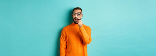 Foto fröhlicher mann, der nach etwas sucht, das durch die lupe schaut und glücklich im stehen lächelt