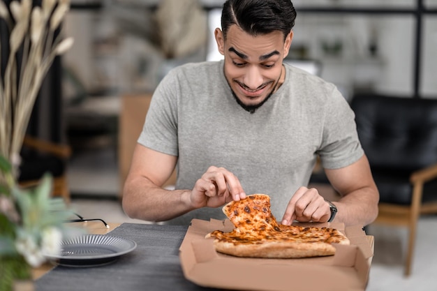 Fröhlicher Mann, der Pizza betrachtet, die eine Scheibe nimmt