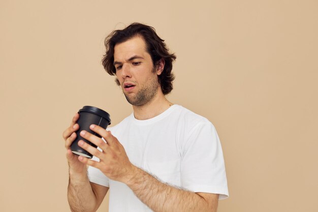 Fröhlicher Mann in einem weißen T-Shirt mit einem schwarzen Glas in der Hand beige Hintergrund