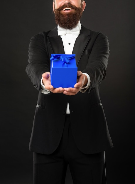 Fröhlicher Mann in Smoking-Fliege auf schwarzem Hintergrund, der geschäftliche Belohnungsbox-Anlassgrüße präsentiert