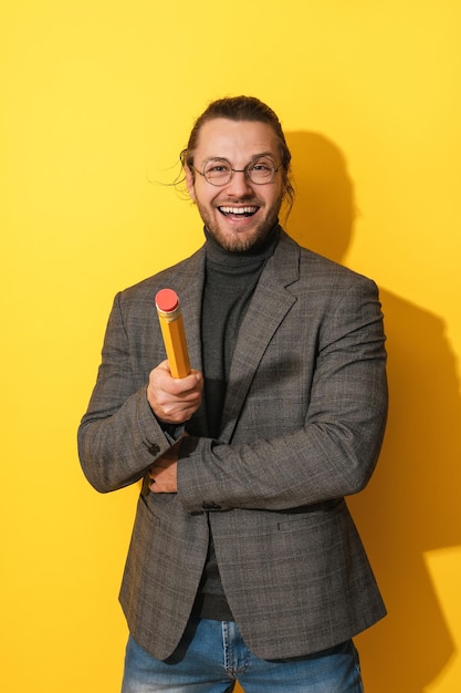 Fröhlicher Mann mit Brille, der große Stifte auf gelbem Hintergrund hält