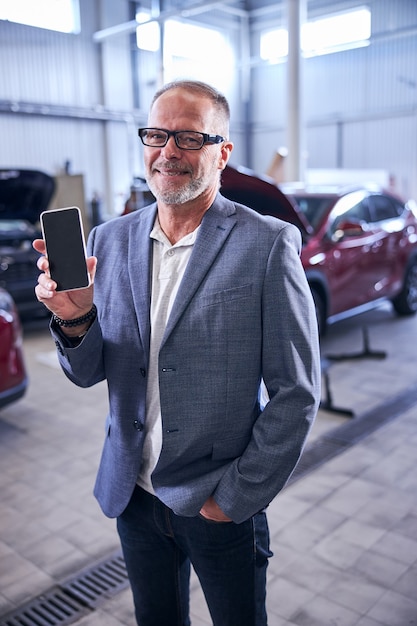 Fröhlicher Mann mit Handy in Autowerkstatt