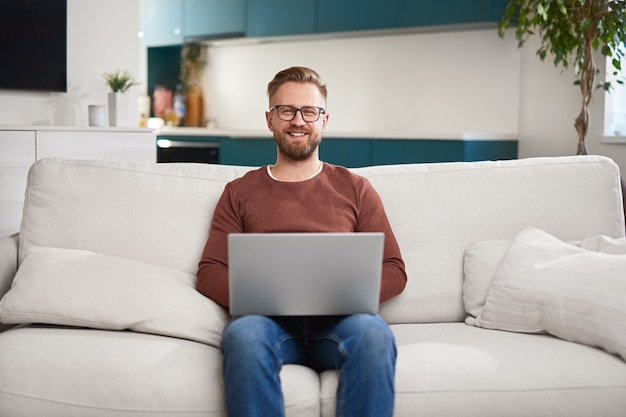 Fröhlicher Mann mit Laptop im Wohnzimmer