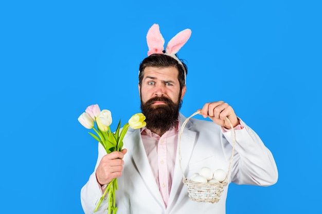 Fröhlicher Osterhasenmann in Hasenohren mit blumenbärtigem Mann im Anzug hält Korb mit Eiern